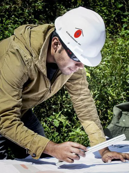 Ingeniero de Alcion Inversiones revisa planos con un escalímetro, con casco de la empresa